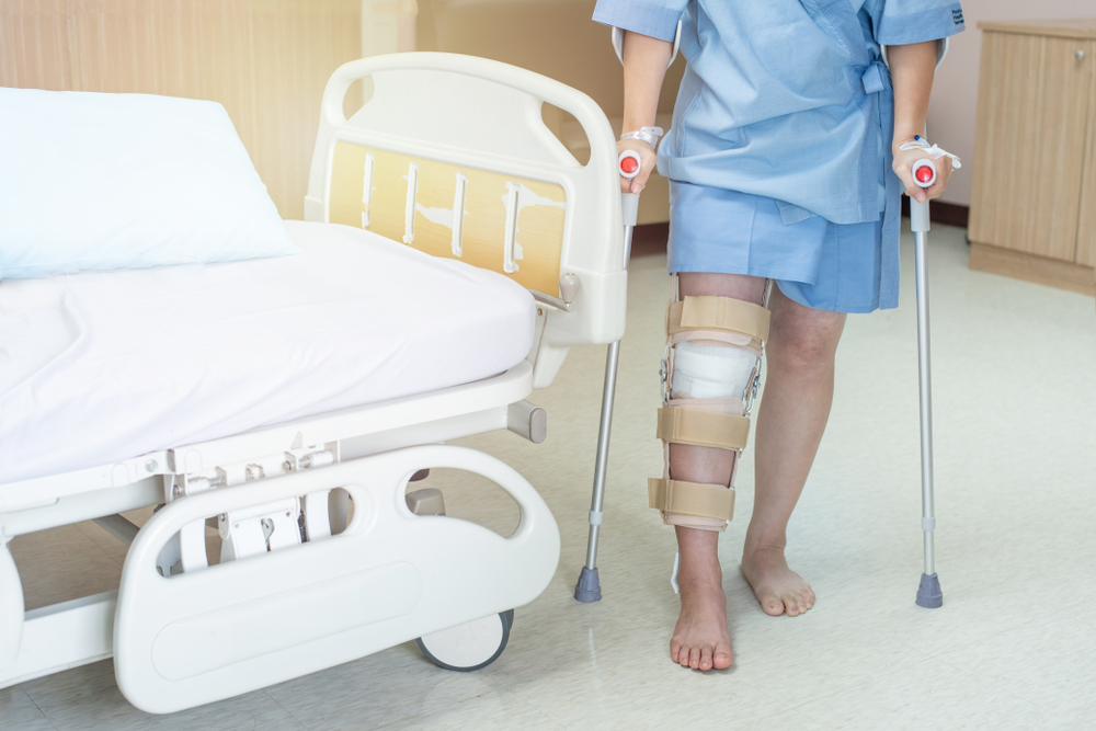 woman patient with knee brace with walking stick in hospital ward