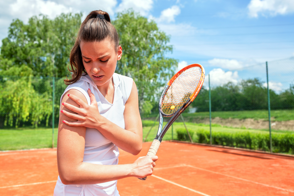 Young woman holding shoulder while playing tennis