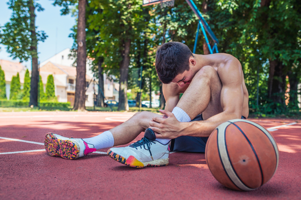 man on ground with ankle injury, basketball beside him